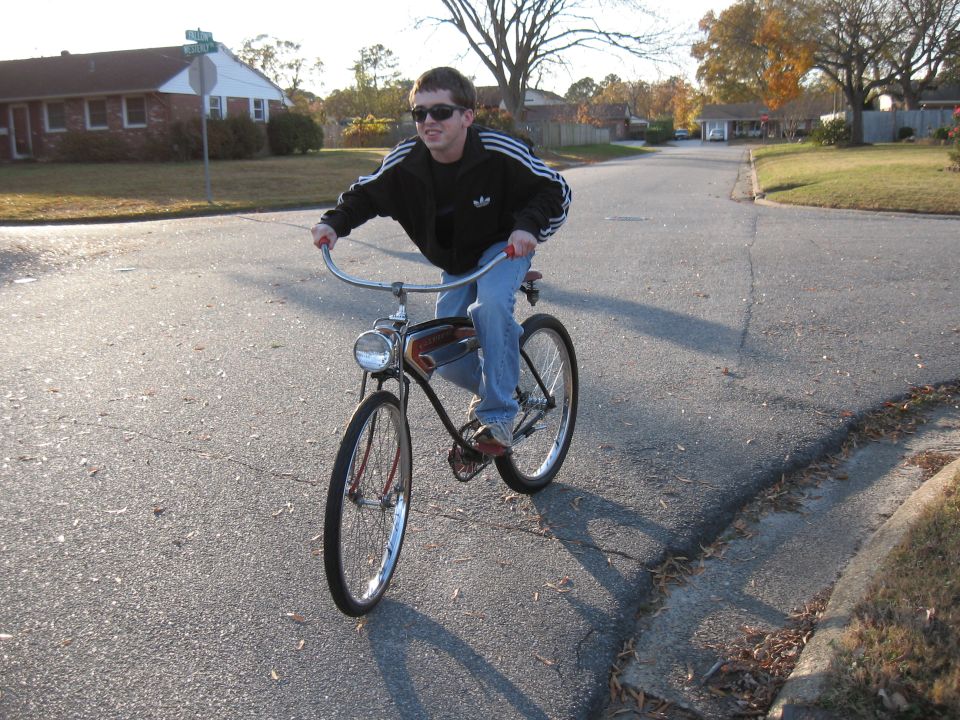 Person in sunglasses and a black jacket riding a vintage bicycle down a suburban street