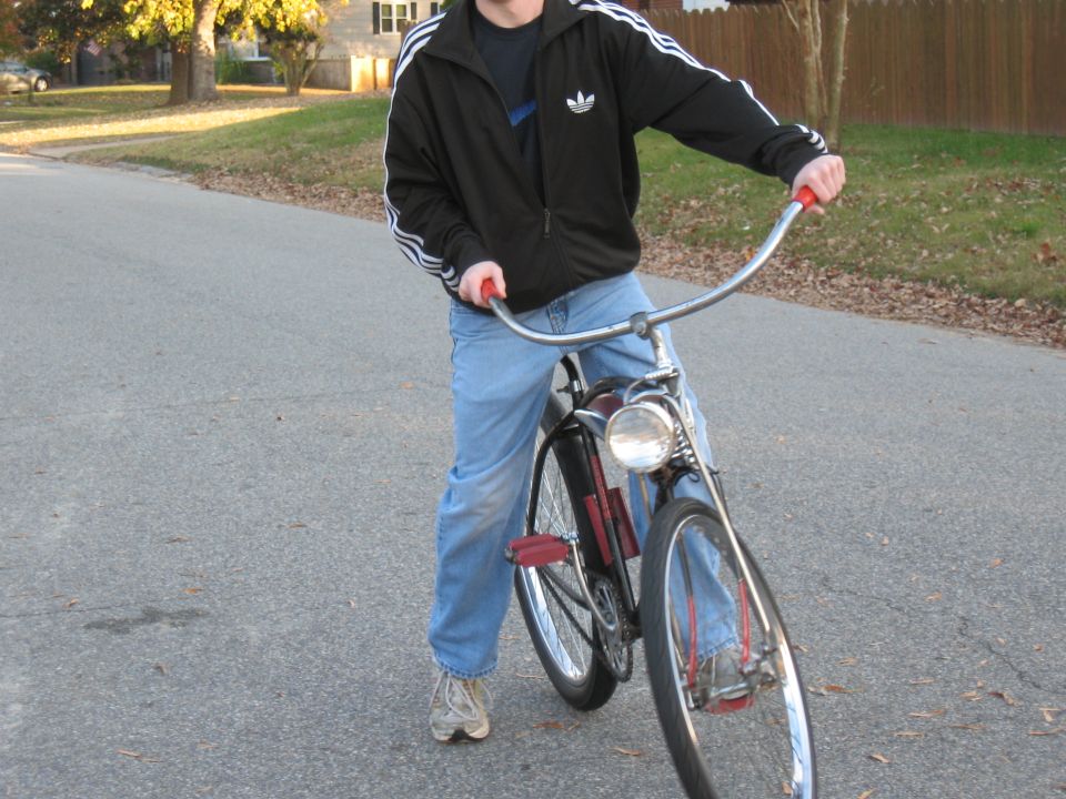 Person in jeans and a black Adidas jacket on a bicycle with a headlight