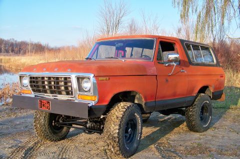 1978 Ford Bronco - This orange 1978 Ford Bronco is shown from a three-quarter front view, with a black bumper and off-road tires.