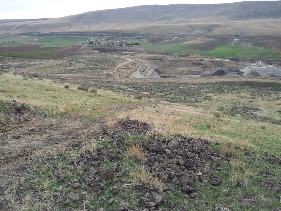 Overcast sky above a barren, hilly landscape with a dirt road leading to a construction site