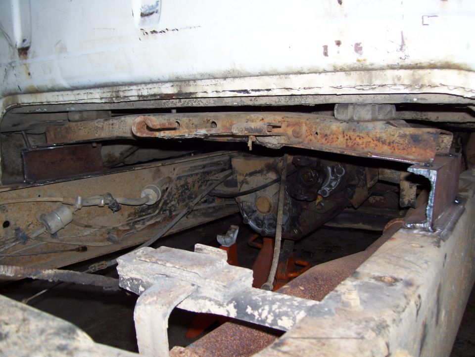 Underside of a white truck frame with rusty drivetrain components and a Supermotors.net watermark