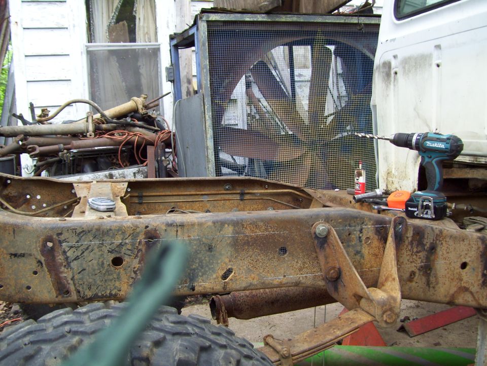 Rusty stripped truck frame with Makita cordless drill and tools on the rail; white cab and shop fan behind