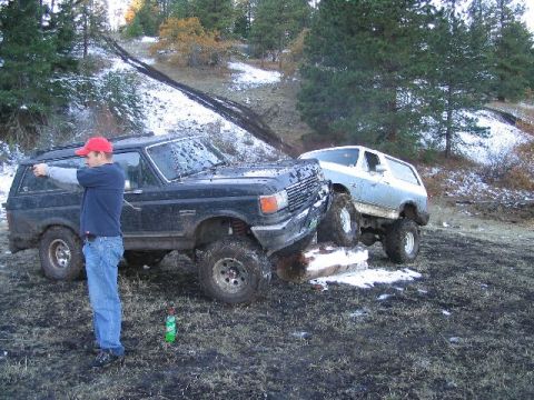 1988 Ford Bronco - Two SUVs are stuck in the mud on a snowy, wooded hill. A man stands by the black SUV.
