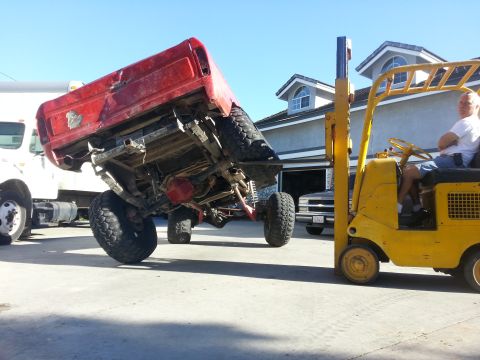 1978 Ford Bronco - A forklift is lifting the rear of a red pickup truck bed while another vehicle is parked in the garage.