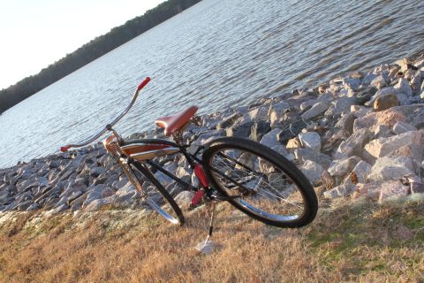 1994 Ford Bronco - A vintage bicycle rests on a rocky embankment beside a calm body of water.
