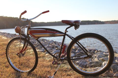 1994 Ford Bronco - A vintage bicycle with a red seat and red grips sits on a rocky shore next to a body of water.