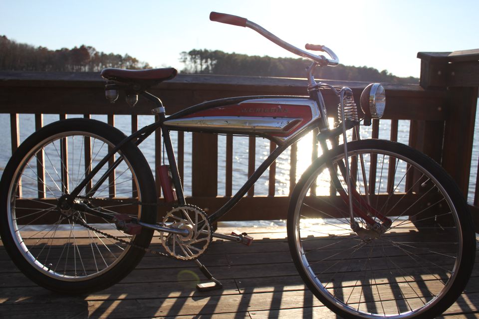 Old bicycle with red seat and handlebars, chrome and red tank, parked on a wooden deck by the water