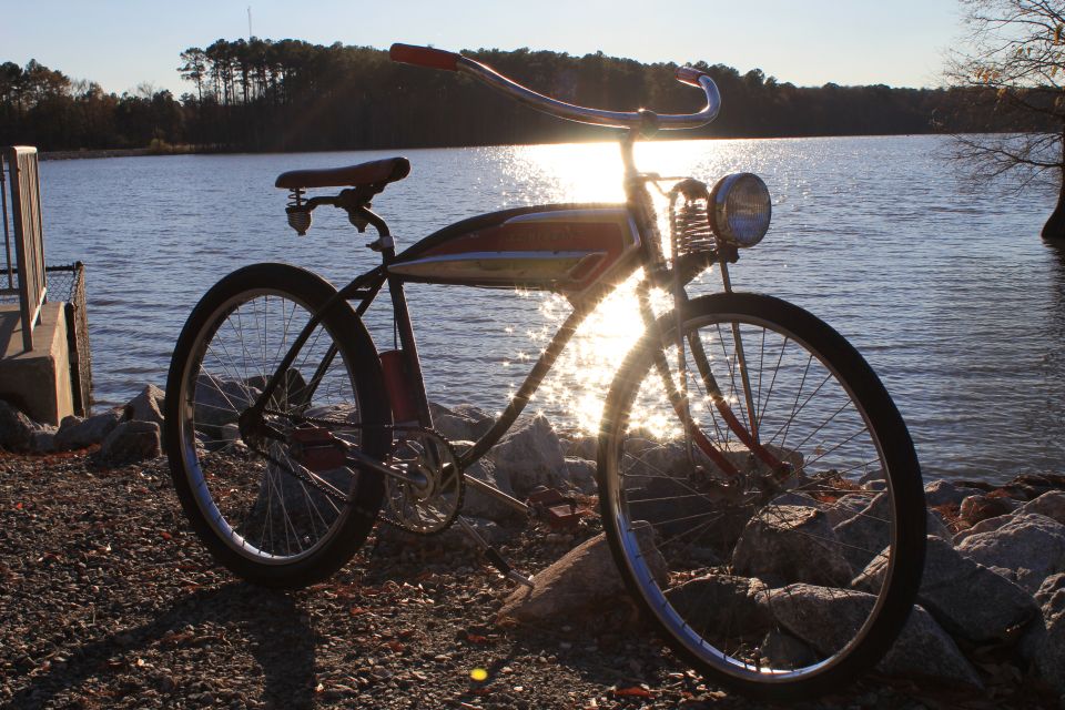 Vintage bicycle with red handlebars and a chrome headlight sits on rocks by a lake