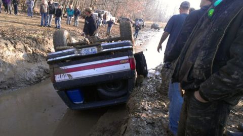 1996 Ford Bronco - This 1996 Ford Bronco has flipped onto its side in a muddy off-road area, with onlookers present.