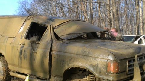 1996 Ford Bronco - A person attempts to free a heavily mud-caked SUV from a wooded area.