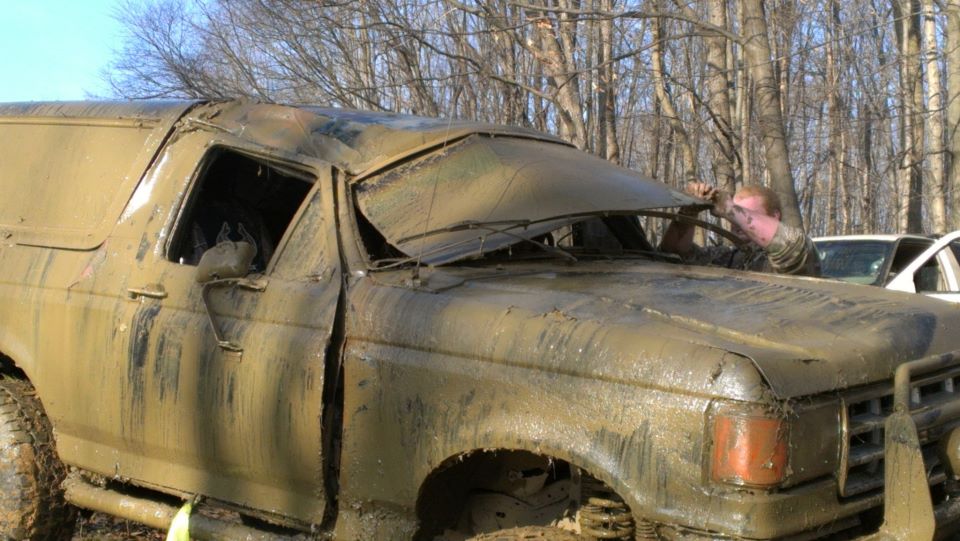 Muddy SUV with a person inside, stuck in trees