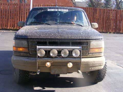 1996 Ford Bronco - 1996 Ford Bronco covered in mud, showing its front grille and driving lights.