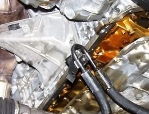 1999 BMW 5 Series - Close-up of an engine's oil pan area with a wrench attached to a bolt.