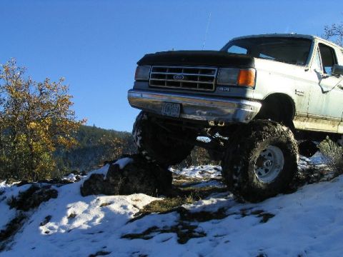 1988 Ford Bronco - This lifted 1988 Ford Bronco navigates a snowy, rocky incline under a clear blue sky.