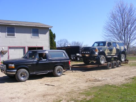 1996 Ford Bronco - A black 1996 Ford Bronco tows a camouflage-painted SUV loaded onto a trailer.