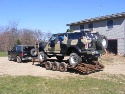 1996 Ford Bronco - Two Ford Broncos are parked outside a house, with one loaded onto a trailer.