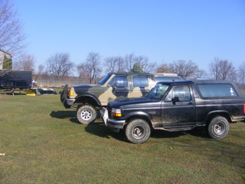 1996 Ford Bronco - Two SUVs are parked on a grassy field under a clear blue sky.