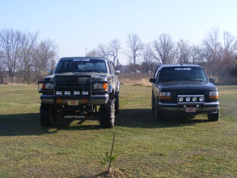 1996 Ford Bronco - Two Ford SUVs, one olive green and one black, are parked side-by-side on a grassy field.
