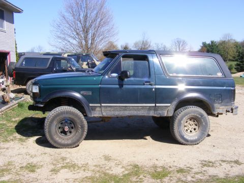 1996 Ford Bronco - A dark green Ford Bronco is parked next to other vehicles under a clear sky.