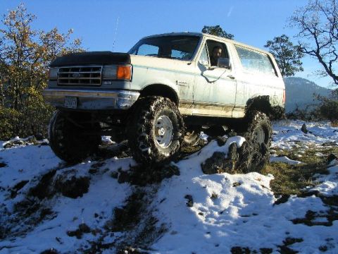 1988 Ford Bronco - Ford Bronco navigates a snowy, rocky trail with large off-road tires.