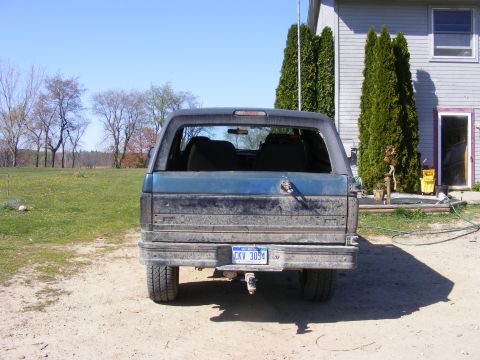 1996 Ford Bronco - This SUV, possibly a Ford Bronco, is seen from the rear in a rural setting. The vehicle appears dusty and has a license plate visible.
