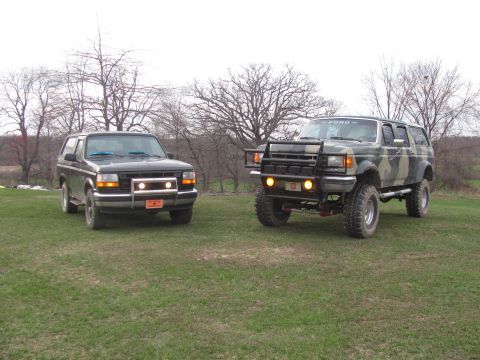1996 Ford Bronco - Two Ford Broncos are parked on a grassy field with trees in the background.