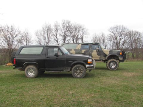 1996 Ford Bronco - A black 1996 Ford Bronco is parked on a grassy field next to a camouflage Ford F-Series truck.