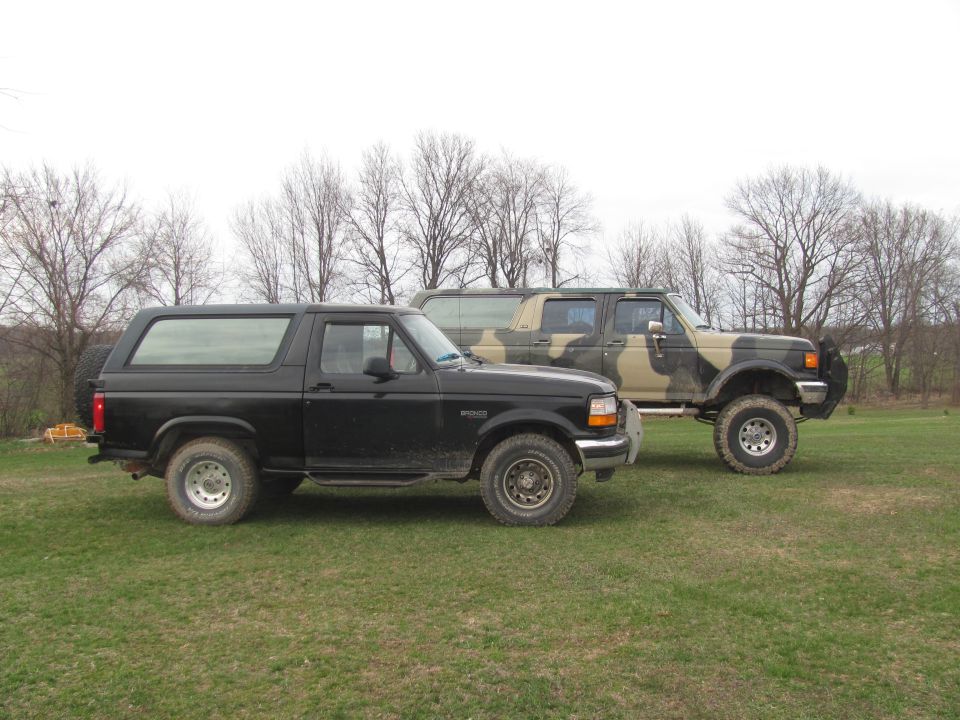 Black 1996 Ford Bronco parked next to a camouflage Ford F-Series truck