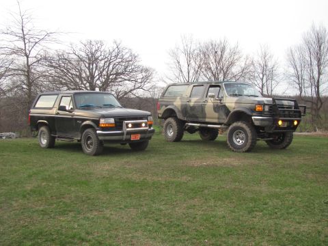 1996 Ford Bronco - Two Ford Broncos are parked side-by-side on a grassy field with trees in the background.