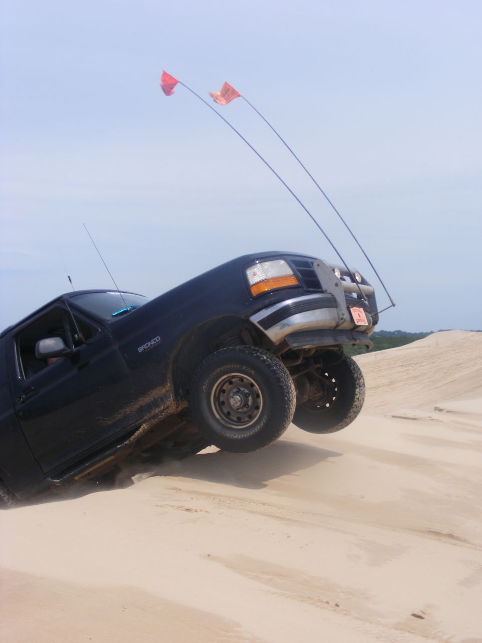 1996 Ford Bronco tilted on a sand dune with two orange flags on poles attached to the roof