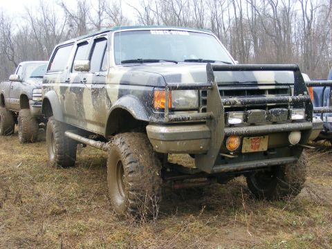 1996 Ford Bronco - Off-road modified Ford Bronco in camouflage paint, seen in a muddy field with other vehicles.