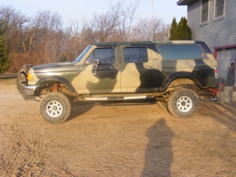 1996 Ford Bronco - Side view of a modified four-door Ford Bronco with camouflage paint and lifted suspension.