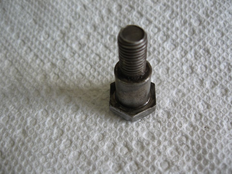 Metal bolt with hexagonal head and threaded shaft, resting on a white textured surface