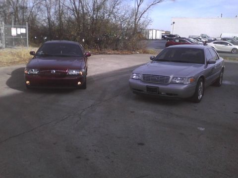 2003 Ford Crown Victoria - A 2003 Ford Crown Victoria is parked next to a maroon sedan in an outdoor lot.