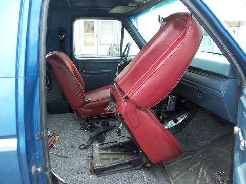 1985 Ford Bronco - The interior of a blue truck shows red bucket seats with the driver's seat tilted forward.