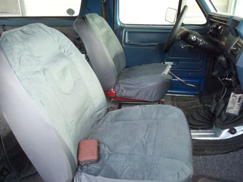 1985 Ford Bronco - The interior of this vehicle features blue door panels and cloth seat covers over the front seats. A steering wheel and gear shifter are vi…