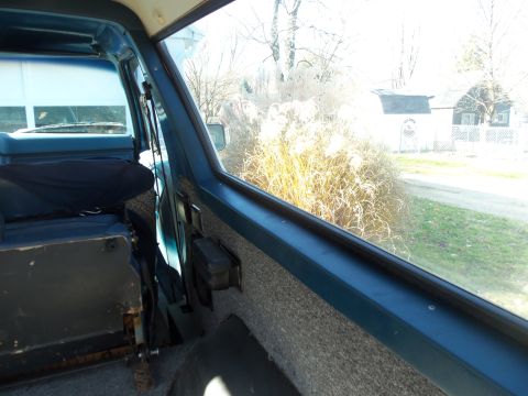 1985 Ford Bronco - View from inside a vehicle shows dry grass and a house through the window.