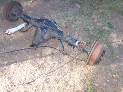 1990 Ford Bronco - This is a rear axle assembly, likely from a truck or SUV, with drum brakes and a shock absorber attached.