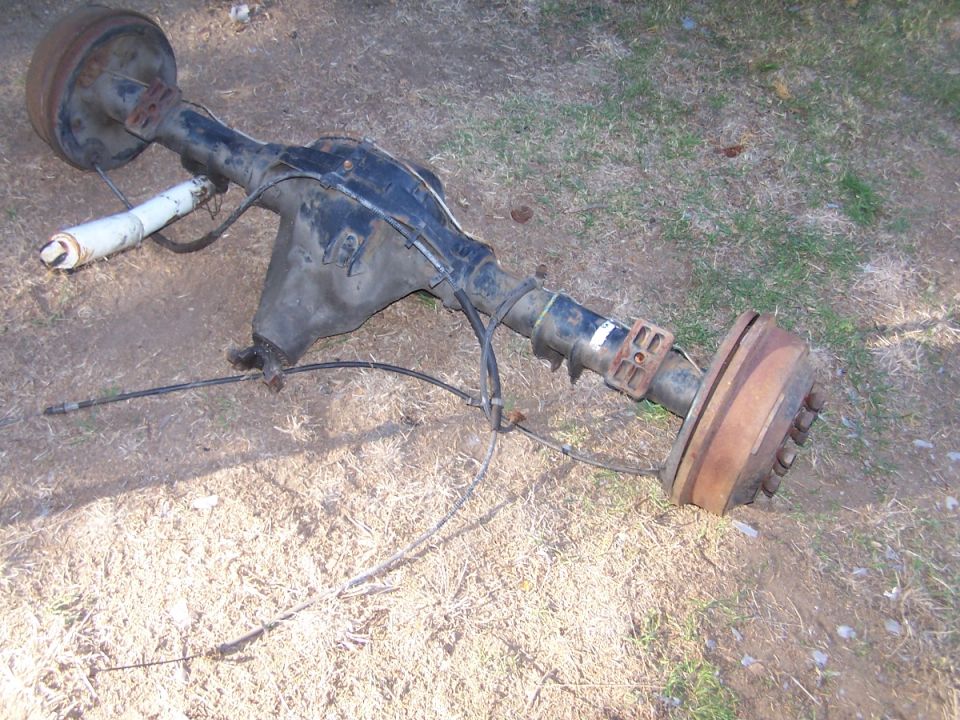 Rear axle assembly with drum brakes and a white shock absorber, lying on the ground