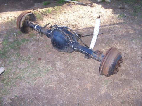 1990 Ford Bronco - A vehicle's rear axle assembly, complete with drum brakes and a shock absorber, rests on the dirt ground.
