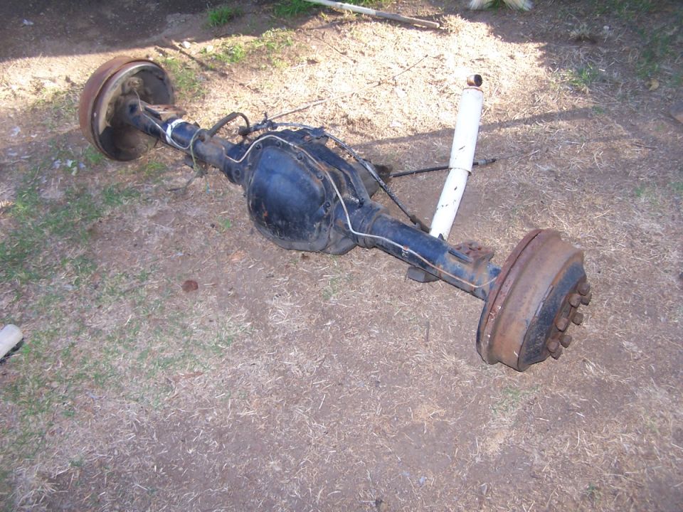 Rear axle assembly with drum brakes and a white shock absorber, lying on the ground