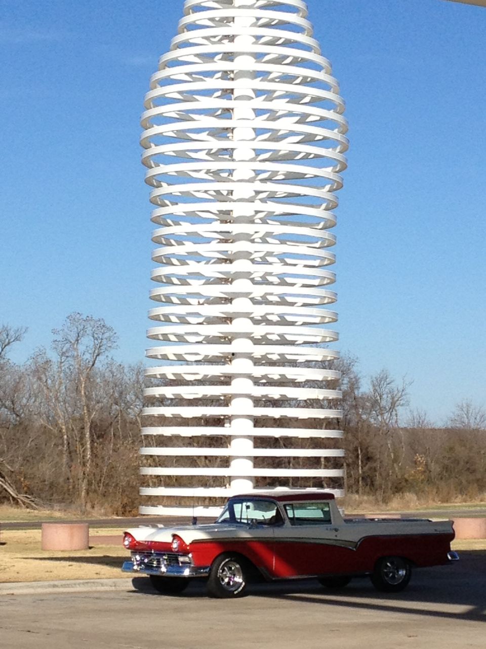 Red and white 1957 Ford Ranchero in side view parked before a tall white ringed tower structure