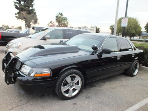 2003 Ford Crown Victoria - Lowered black Panther-platform sedan with chrome multi-spoke wheels and exposed front bumper bracket in a parking lot