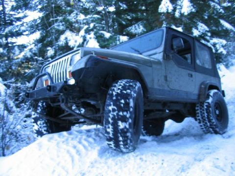 1988 Ford Bronco - A Jeep Wrangler YJ navigates a snowy trail surrounded by snow-covered trees.