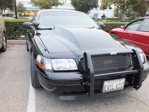 2003 Ford Crown Victoria - Front three-quarter of a black Crown Victoria with brush guard and EVIL VIC plate parked beside a red sedan