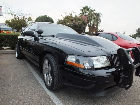 2003 Ford Crown Victoria - Glossy black Crown Victoria seen from the front fender, chrome five-spoke wheel and partial grille guard