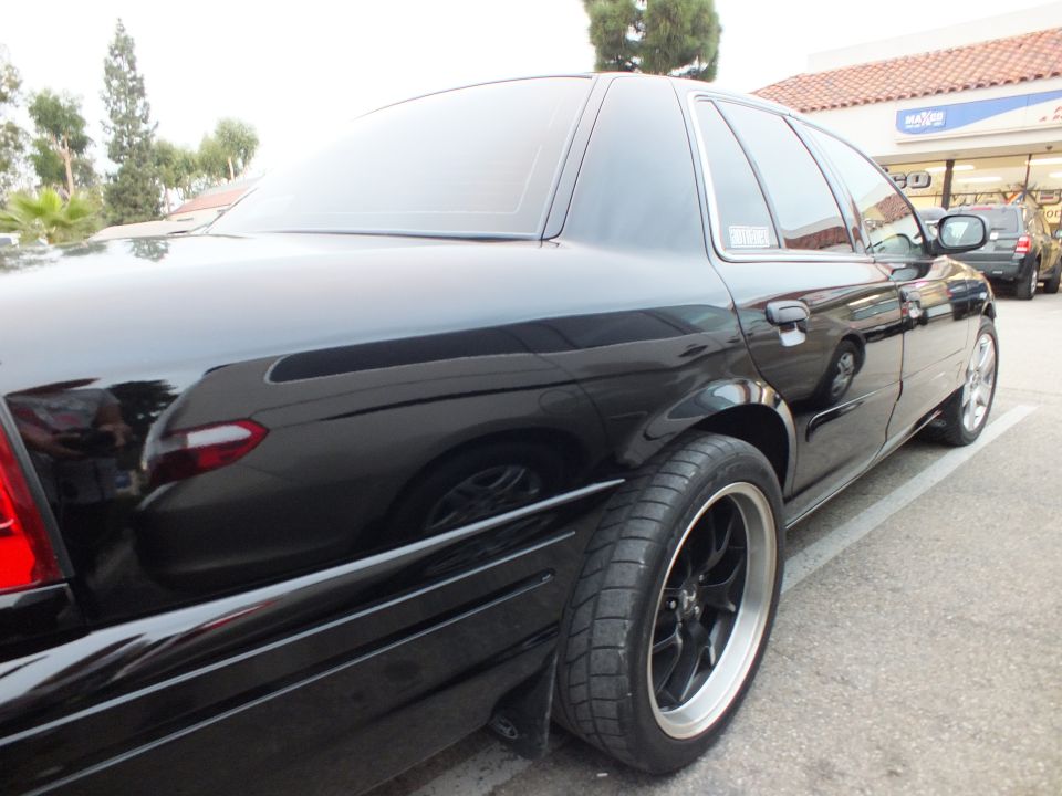 Rear quarter of black Ford Crown Victoria sedan with black mesh wheels and tinted windows