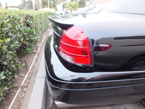 2003 Ford Crown Victoria - Close-up of a Crown Victoria right tail light and decklid, glossy black paint beside a trimmed hedge
