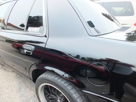 2003 Ford Crown Victoria - Side view of a black Crown Victoria rear door, fuel filler and quarter window decal, black wheel below