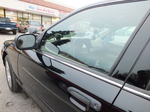 2003 Ford Crown Victoria - Side mirror and front door window of a black Crown Victoria revealing a tan dashboard and steering wheel